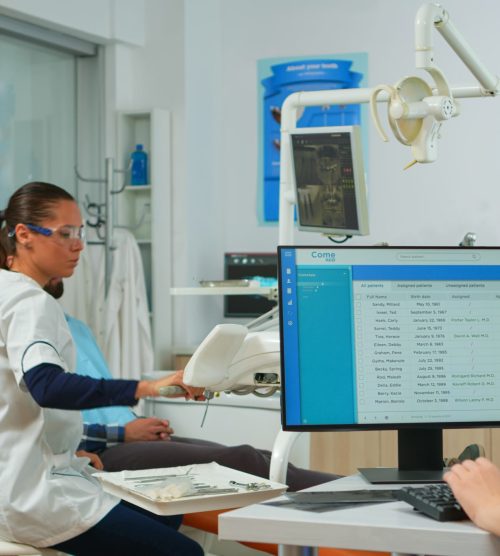 nurse-typing-computer-making-appointments-while-dental-specialist-talking-patient-stomatology-chair-before-examination-dentist-nurse-working-together-modern-stomatological-clinic (1)